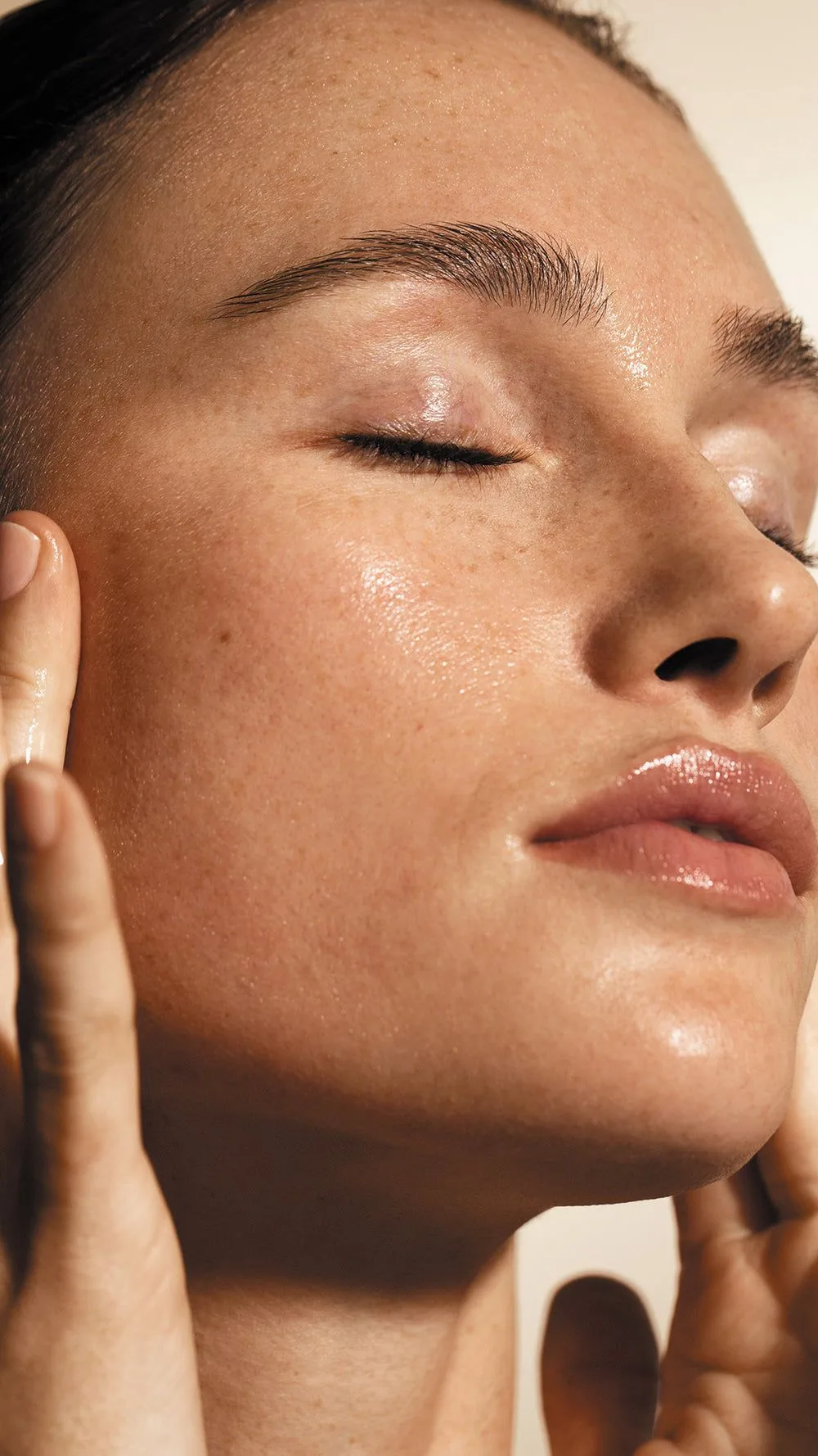 Rosto de perto de mulher de olhos fechados, pele iluminada e brilhante